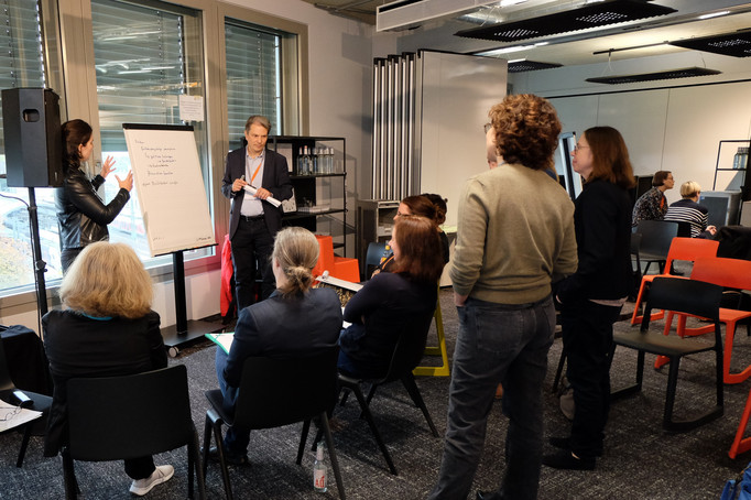 Thorsten Halling und Annegret Dreher stehen an einem Flipchart und diskutieren mit Teilnehmer*innen.