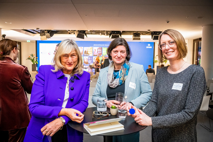 Drei Frauen stehen an einem Tisch und unterhalten sich.